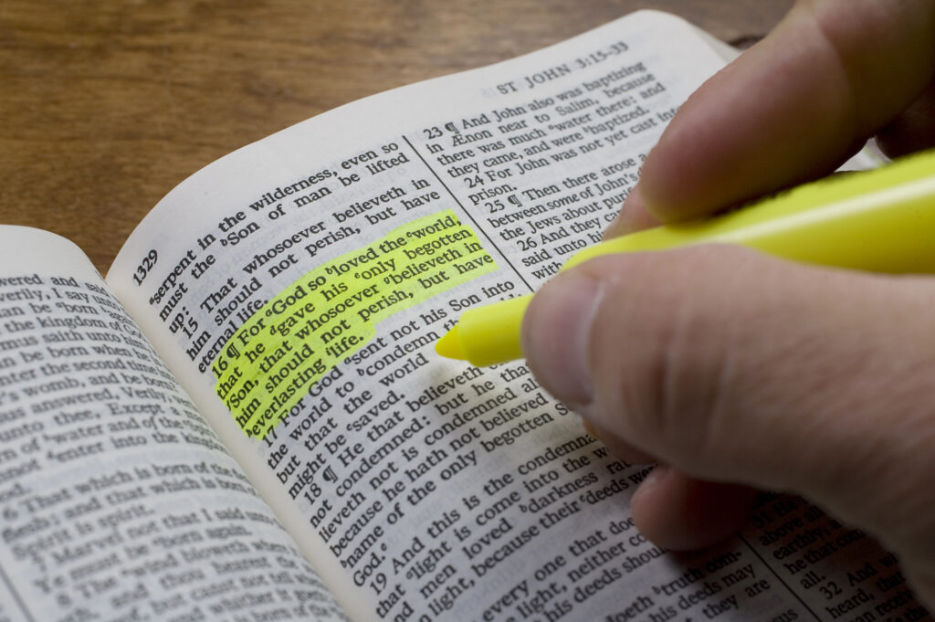 A man uses a highlighter to mark a bible verse, John 3:16.
