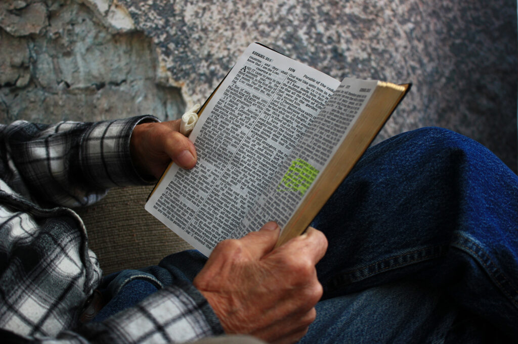 Old man sitting in an armchair reading the bible in casual clothing