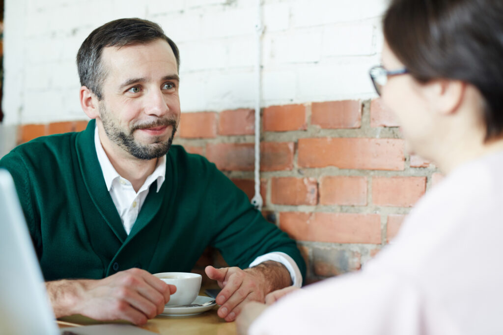 Portrait of two business people, mature man and woman, dressed in smart casual wear looking at each other and smiling during meeting in cafe