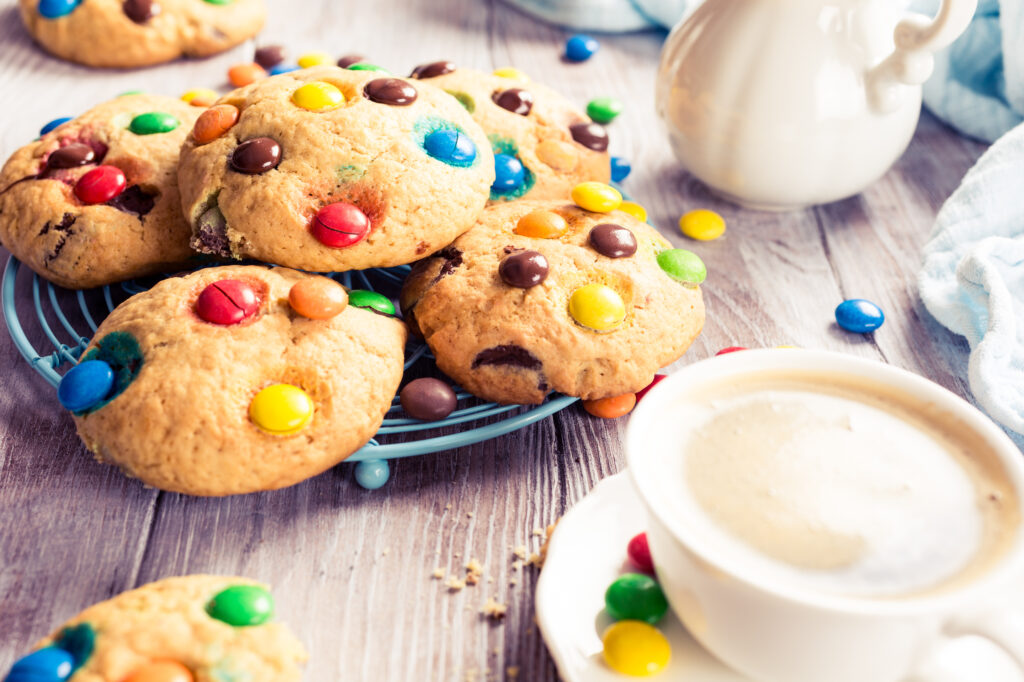 Homemade cookies with colorful chocolate candies with cup coffee on old white wooden table. Retro style toned.